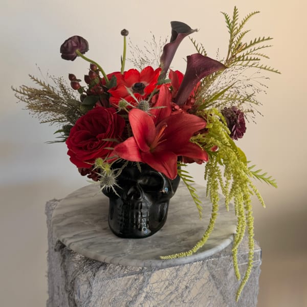 Red and purple floral arrangement in a black skull vase