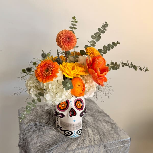 Orange and yellow flowers arranged in a decorated skull vase