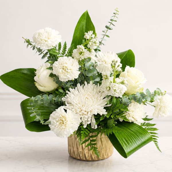 White flowers arranged in a gold vase with broad green leaves