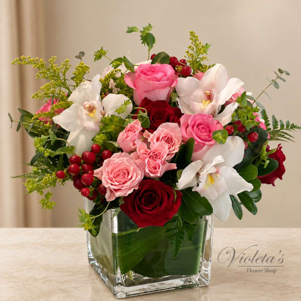 Pink and red roses with white orchids in a clear square vase