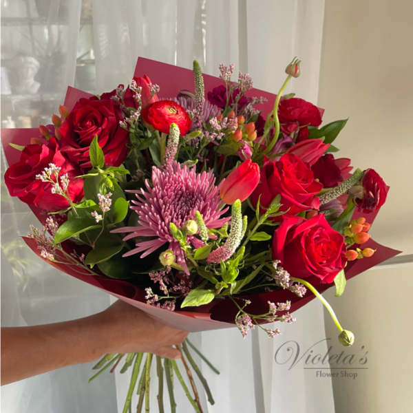 Handheld bouquet of red roses and pink mixed flowers wrapped in burgundy paper