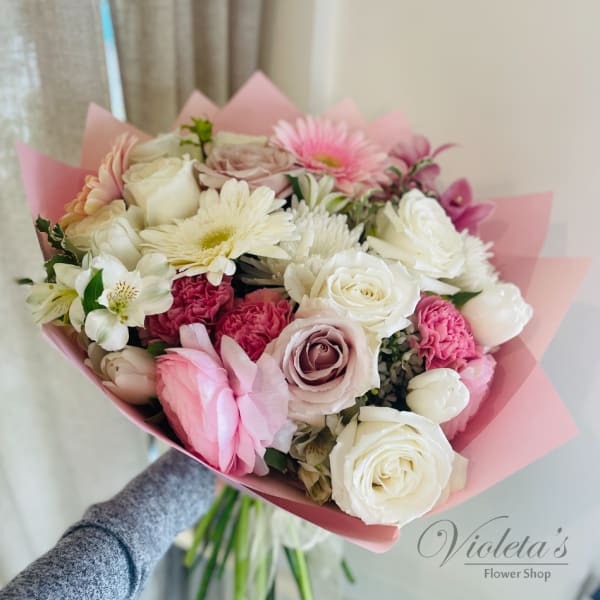 Handheld bouquet of pink and white roses with mixed blooms wrapped in pink paper