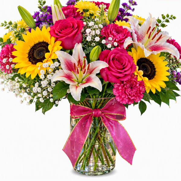 Bouquet of sunflowers, pink roses, and lilies in a glass vase with a pink ribbon