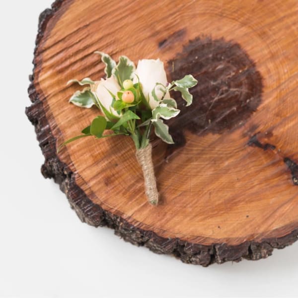 Small white boutonniere with berries and variegated greenery on wood