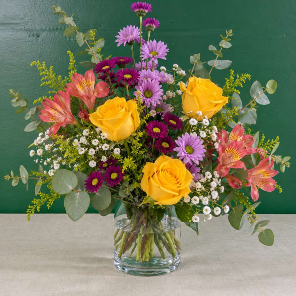 Mixed bouquet of yellow roses and pink flowers in a glass vase