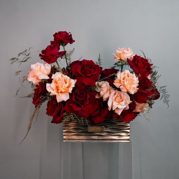Red and peach roses arranged in a metallic rectangular container
