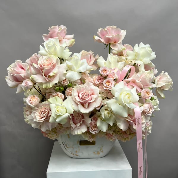 Pink and white roses arranged in a white vase with a pink ribbon
