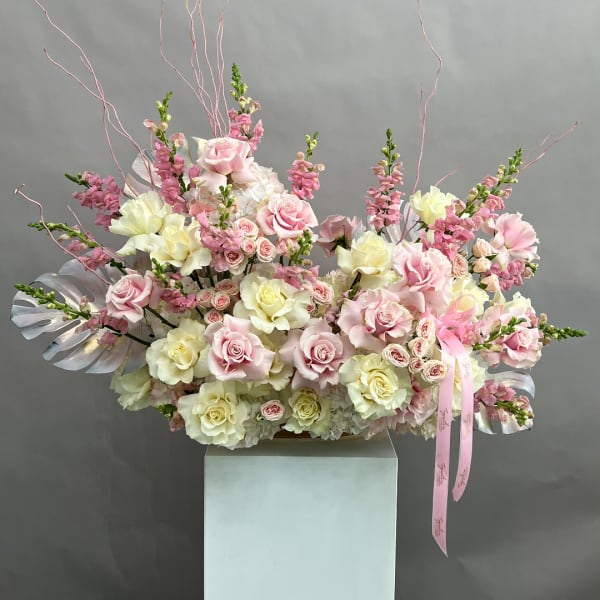 Large pink and white rose arrangement in a vase with ribbon accents