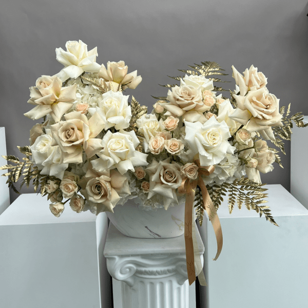 Cream rose arrangement in a white vase with gold foliage accents