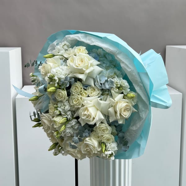 Bouquet of white roses and pale blooms wrapped in light blue paper