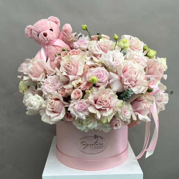 Pink teddy bear in a box with pale pink roses and carnations