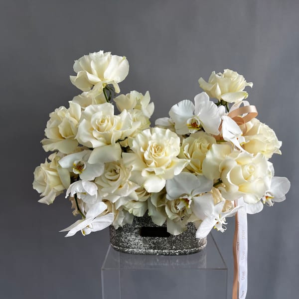 Cream rose and white orchid arrangement in a textured dark container