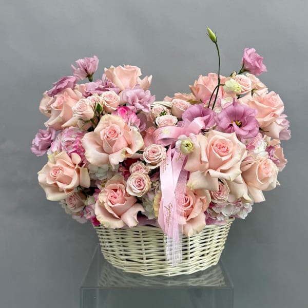 Pink roses and lisianthus arranged in a white wicker basket