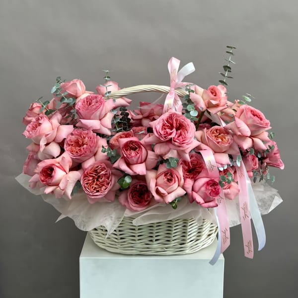 Pink roses arranged in a white wicker basket with ribbon accents