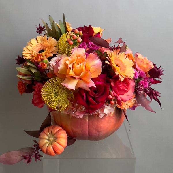 Floral arrangement in a pumpkin-shaped container with roses and gerbera daisies