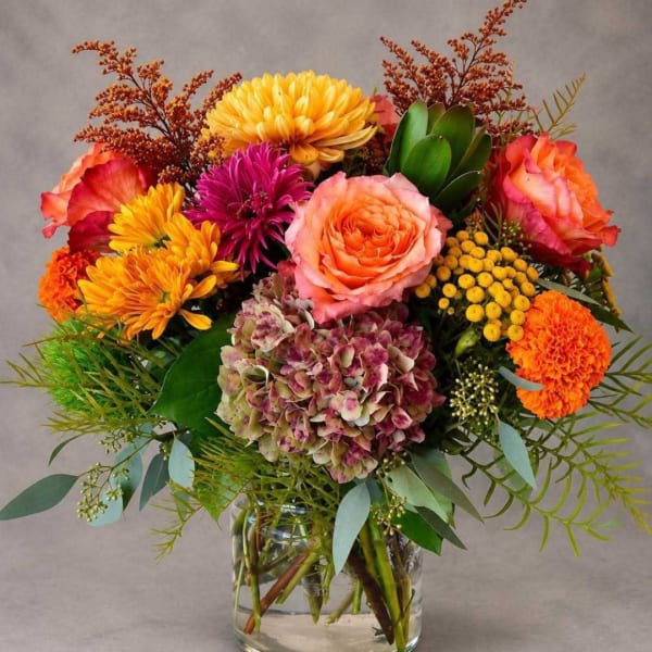 Colorful bouquet of roses, chrysanthemums, hydrangea, and marigolds in a glass vase