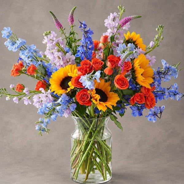 Bouquet of sunflowers, roses, and blue flowers in a clear glass vase