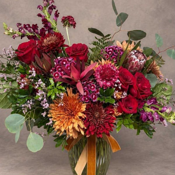 Mixed bouquet of red, purple, and orange flowers in a glass vase