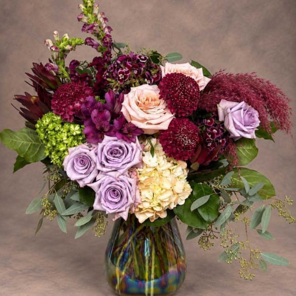 Mixed bouquet of roses, hydrangea, and burgundy blooms in a glass vase