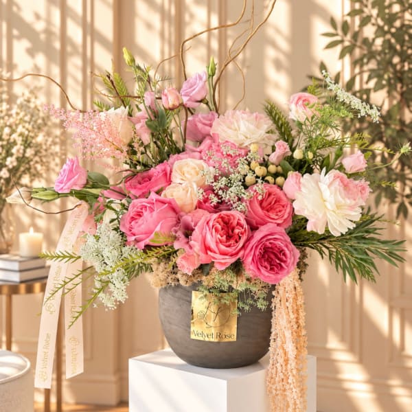 Pink and white rose arrangement in a dark vase with trailing ribbon