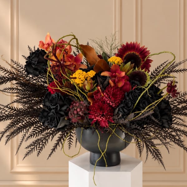 Dark floral arrangement with red and orange blooms in a black vase