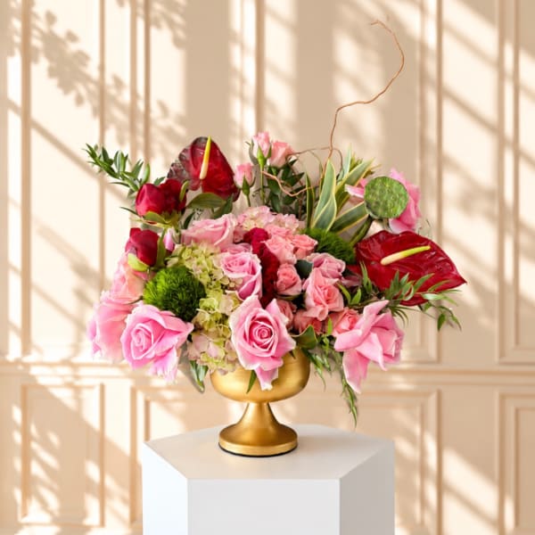 Pink roses and red anthuriums arranged in a gold pedestal vase
