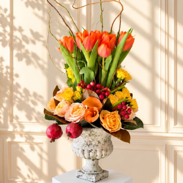 Orange tulips and roses arranged in a white urn vase