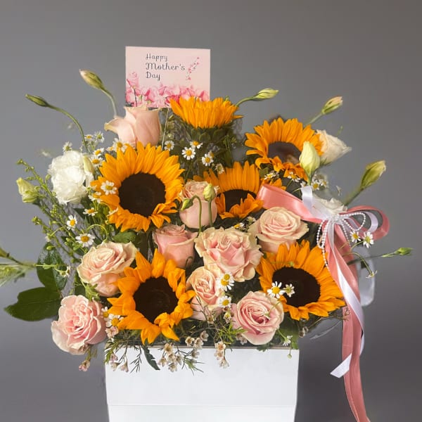 Pink roses and sunflowers arranged in a white box with a Mother's Day card