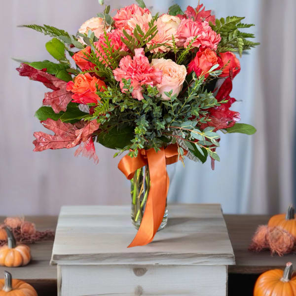 Pink and peach roses with carnations in a glass vase with an orange ribbon