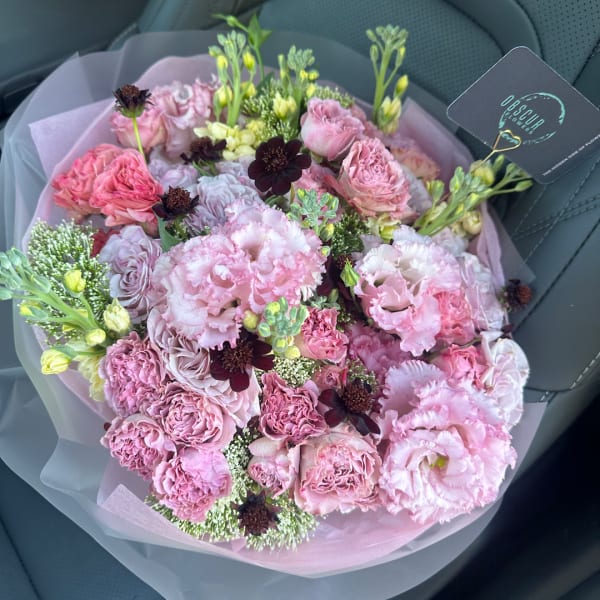 Pink mixed bouquet wrapped in pale paper with a shop tag