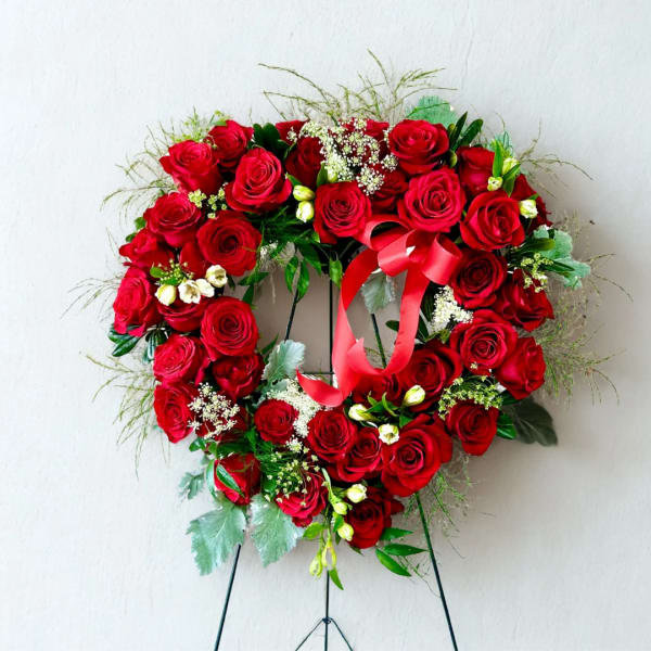 Heart-shaped wreath of red roses with a red ribbon on a stand