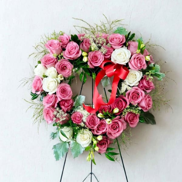 Heart-shaped rose wreath with pink and white roses and a red ribbon