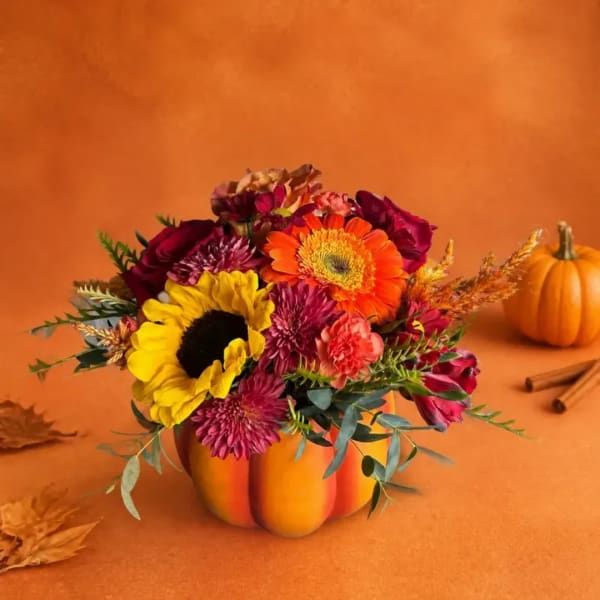 Autumn bouquet in a pumpkin-shaped container with sunflowers and orange blooms