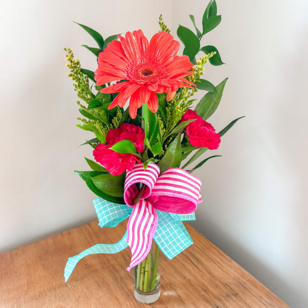 Pink gerbera and carnations in a clear glass vase with striped ribbon