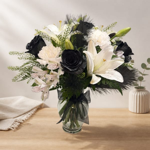 Black and white floral arrangement in a glass vase with lilies and roses