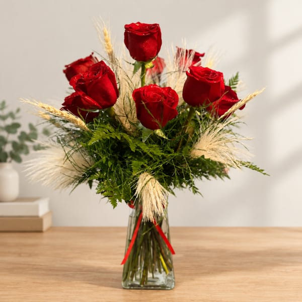Red roses arranged in a clear glass vase with dried grass accents