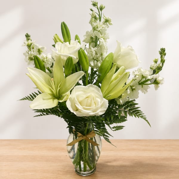 White lilies and roses arranged in a clear glass vase