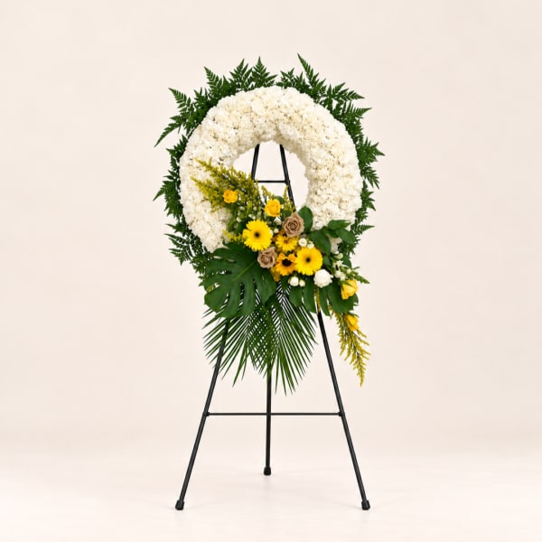 White floral wreath on a black easel with yellow flowers and greenery