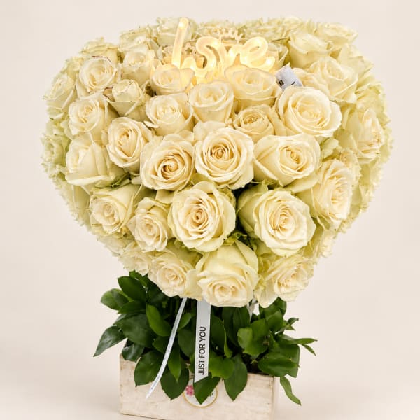 Heart-shaped bouquet of cream roses in a box with a lit "love" sign
