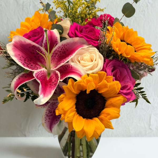 Bouquet of pink roses, sunflowers, and a pink lily in a glass vase