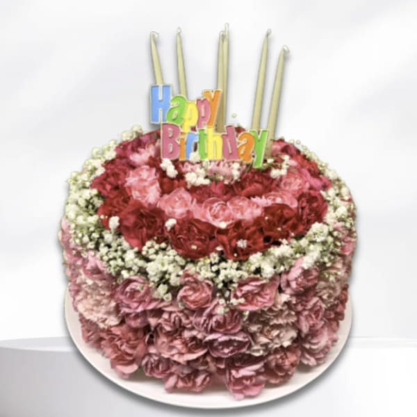 Round pink floral birthday cake with candles and a Happy Birthday topper