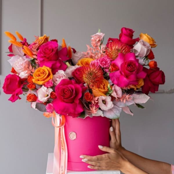 Bright mixed bouquet of roses and orange blooms in a pink hatbox