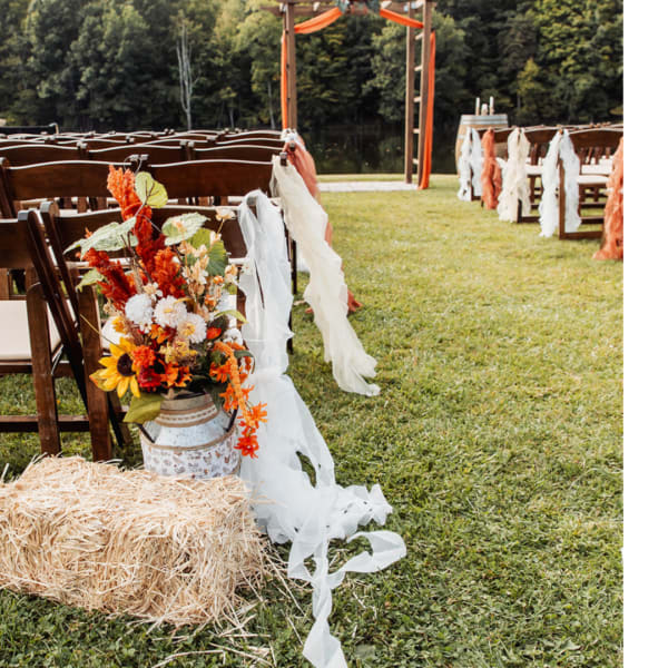Fall floral arrangement in a metal bucket beside decorated wedding chairs
