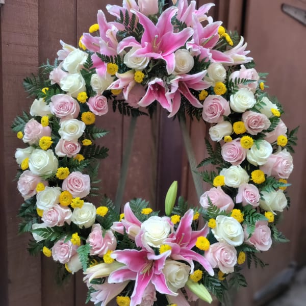 Heart-shaped floral wreath with pink lilies, roses, and yellow accents