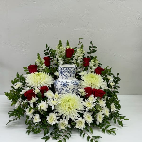 Red roses and white chrysanthemums arranged around a blue-and-white vase