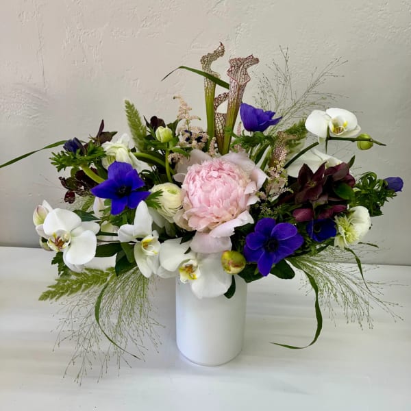 Mixed bouquet with pink peony, white orchids, and purple flowers in a white vase