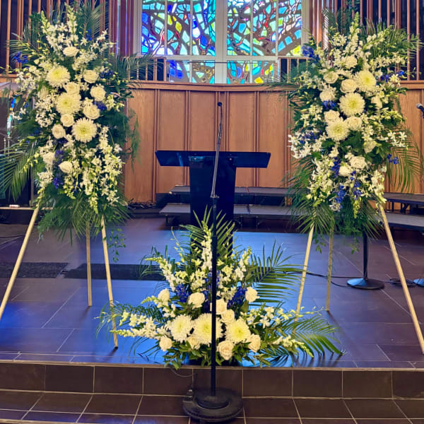 Large white floral arrangements flank a church podium with a smaller matching arrangement in front.