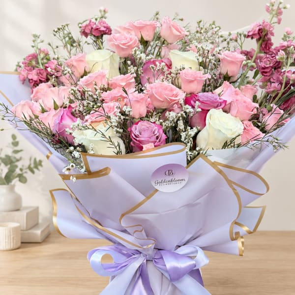 Bouquet of pink and white roses wrapped in lavender paper with a ribbon