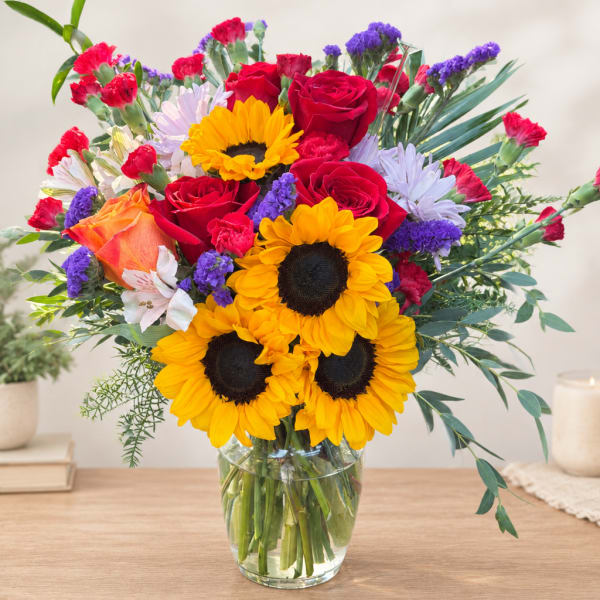 Mixed bouquet with sunflowers, red roses, and carnations in a glass vase