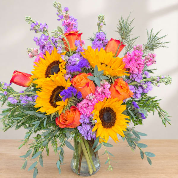 Bouquet of sunflowers, orange roses, and purple flowers in a glass vase